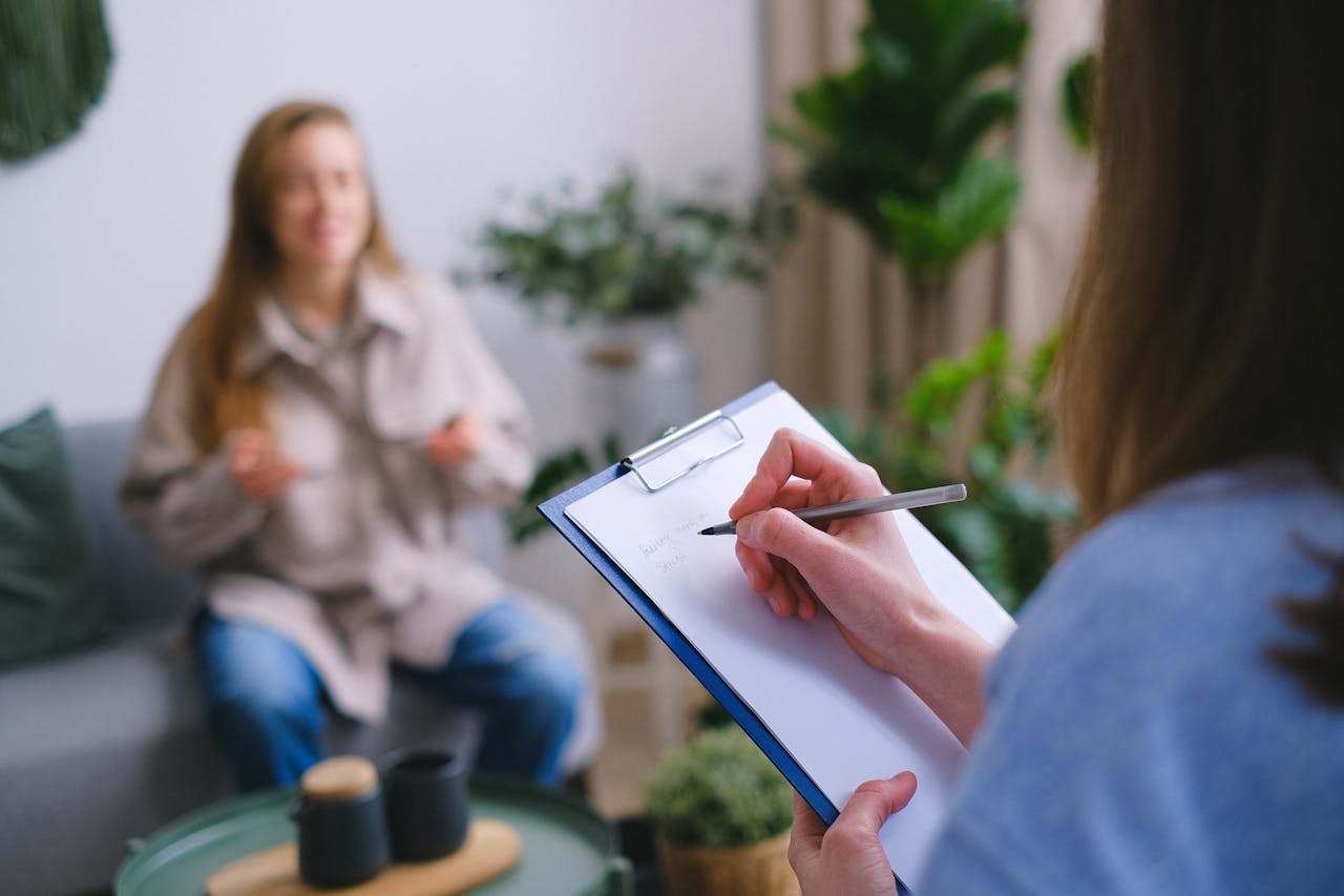 collection-05 Unrecognizable professional female psychologist writing on clipboard while sitting against client on blurred background during psychotherapy session in light office