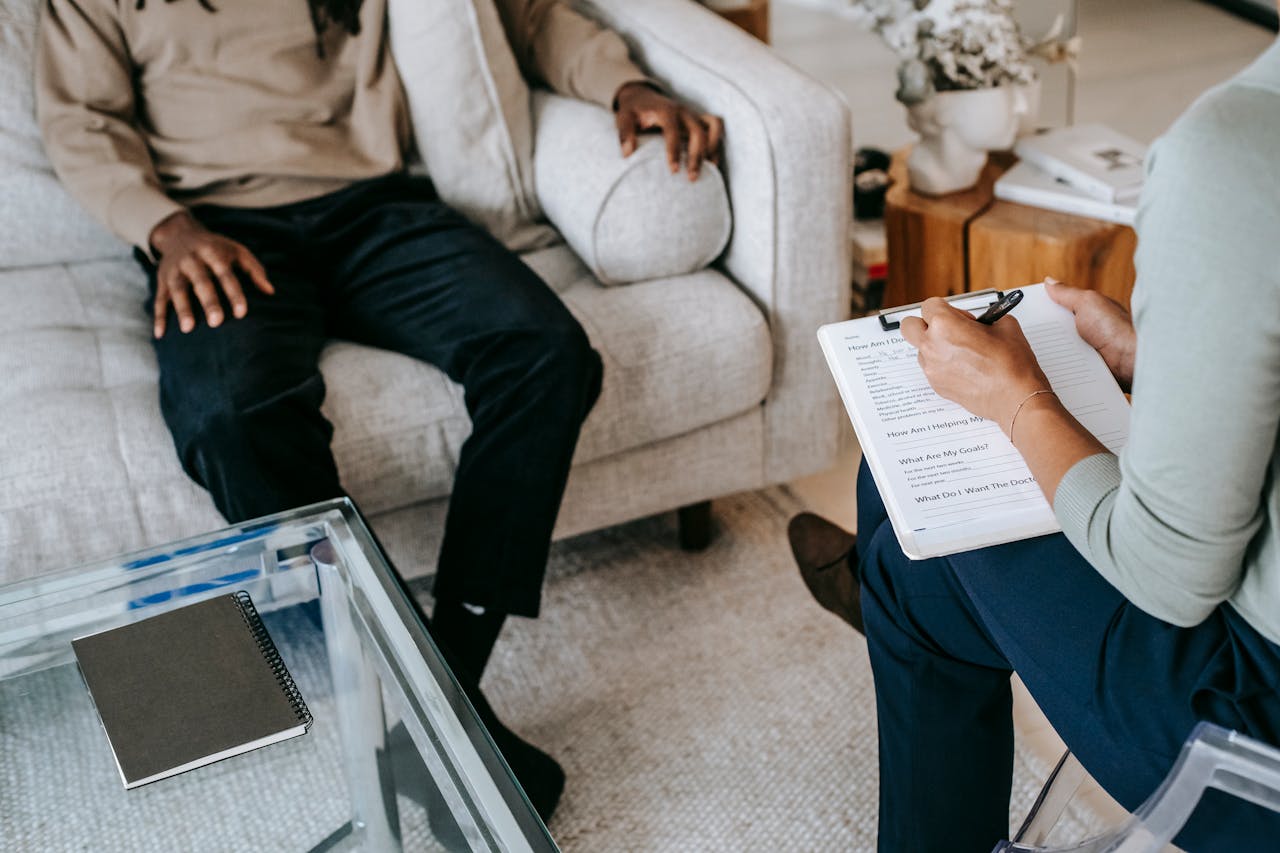 our-story-02 From above crop African American male in casual clothes sitting on comfy couch and answering professional female consultant questions in modern psychotherapy office